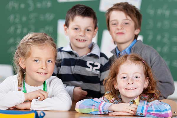 Kinder im ersten Schuljahr an der Schulbank mit Schultafel im Hintergrund