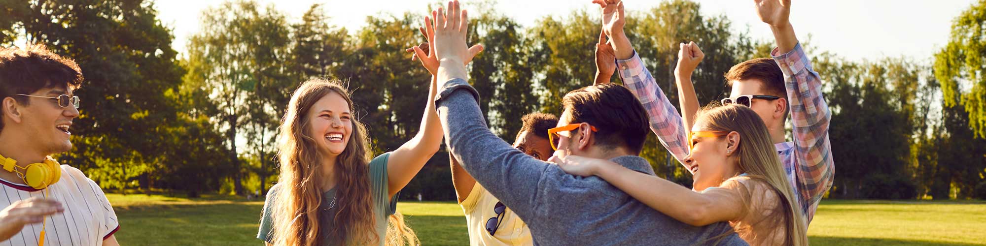 Gruppe junger, fröhlicher Menschen im Park geben sich High-five
